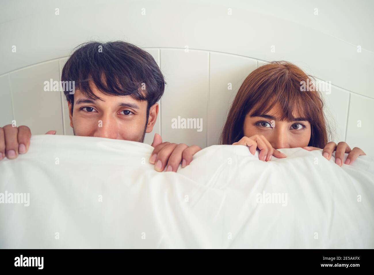 Happy young couple relaxing in home bedroom after waking up in the morning. Stock Photo