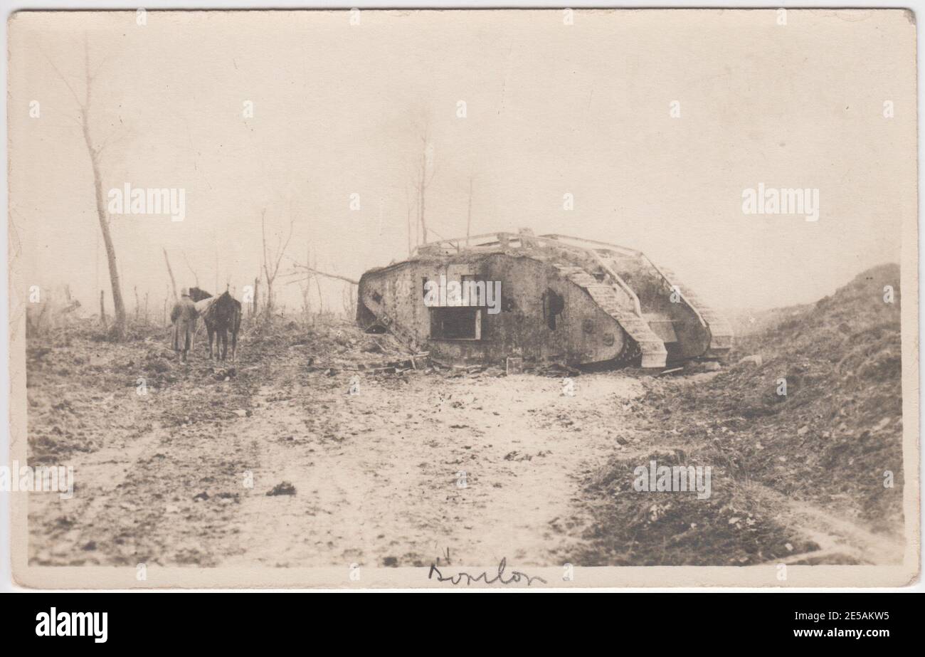 Photograph of a burnt out tank in the mud of a Western Front First World War battlefield. A German soldier is leading a horse past the tank towards bomb damaged trees Stock Photo