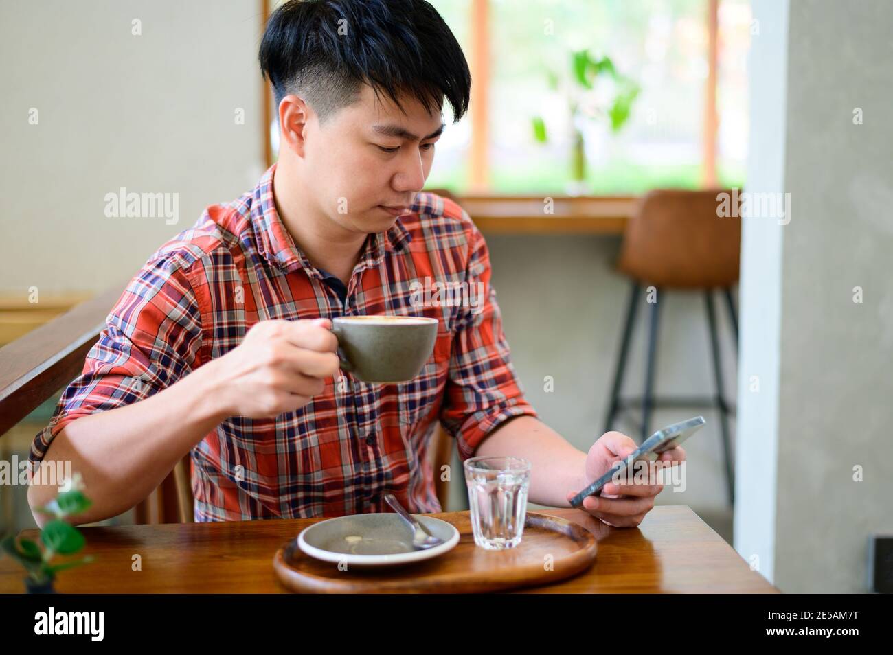 Young asian man using smartphone and having coffee Stock Photo