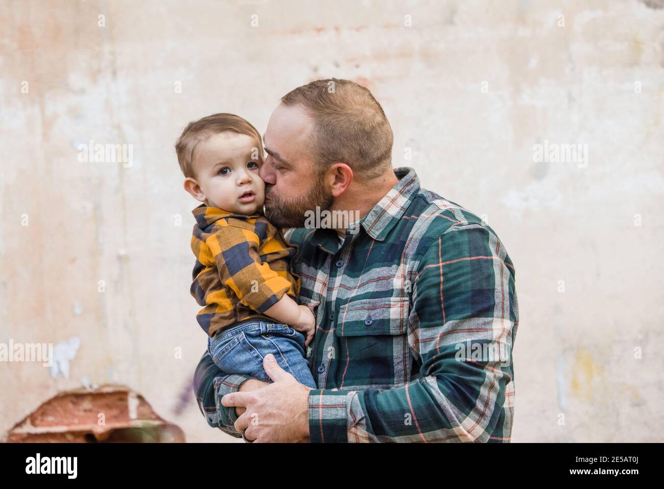 A father and his baby son outside in an urban setting against an old textured wall Stock Photo