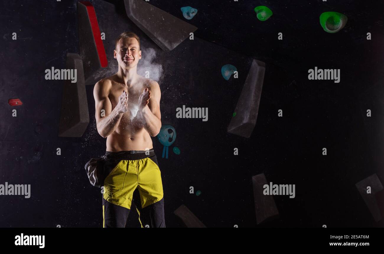 Cheerful young man applying magnesium powder before climbing in bouldering gym Stock Photo
