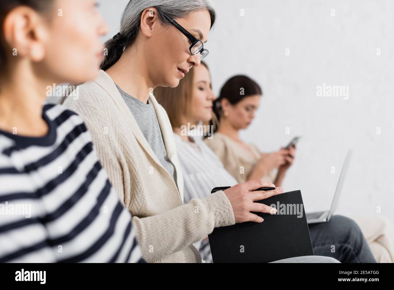 Asian businesswoman in glasses holding pen and notebook near coworkers during lecture Stock Photo