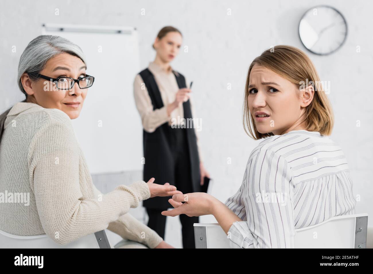 skeptical multicultural businesswomen gesturing while looking at camera during lecture Stock Photo