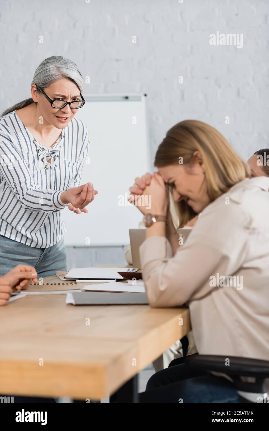 displeased asian team leader gesturing while talking with upset coworker in office Stock Photo