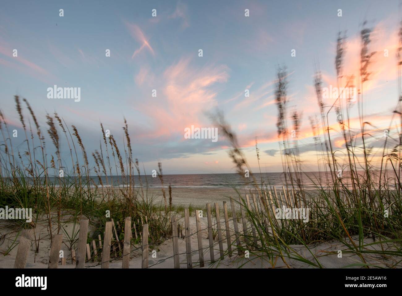 Sunset creates cotton candy skies over the sand dunes at Atlantic Beach, North Carolina. Sea oats sway in the breeze along the path that leads to the Stock Photo
