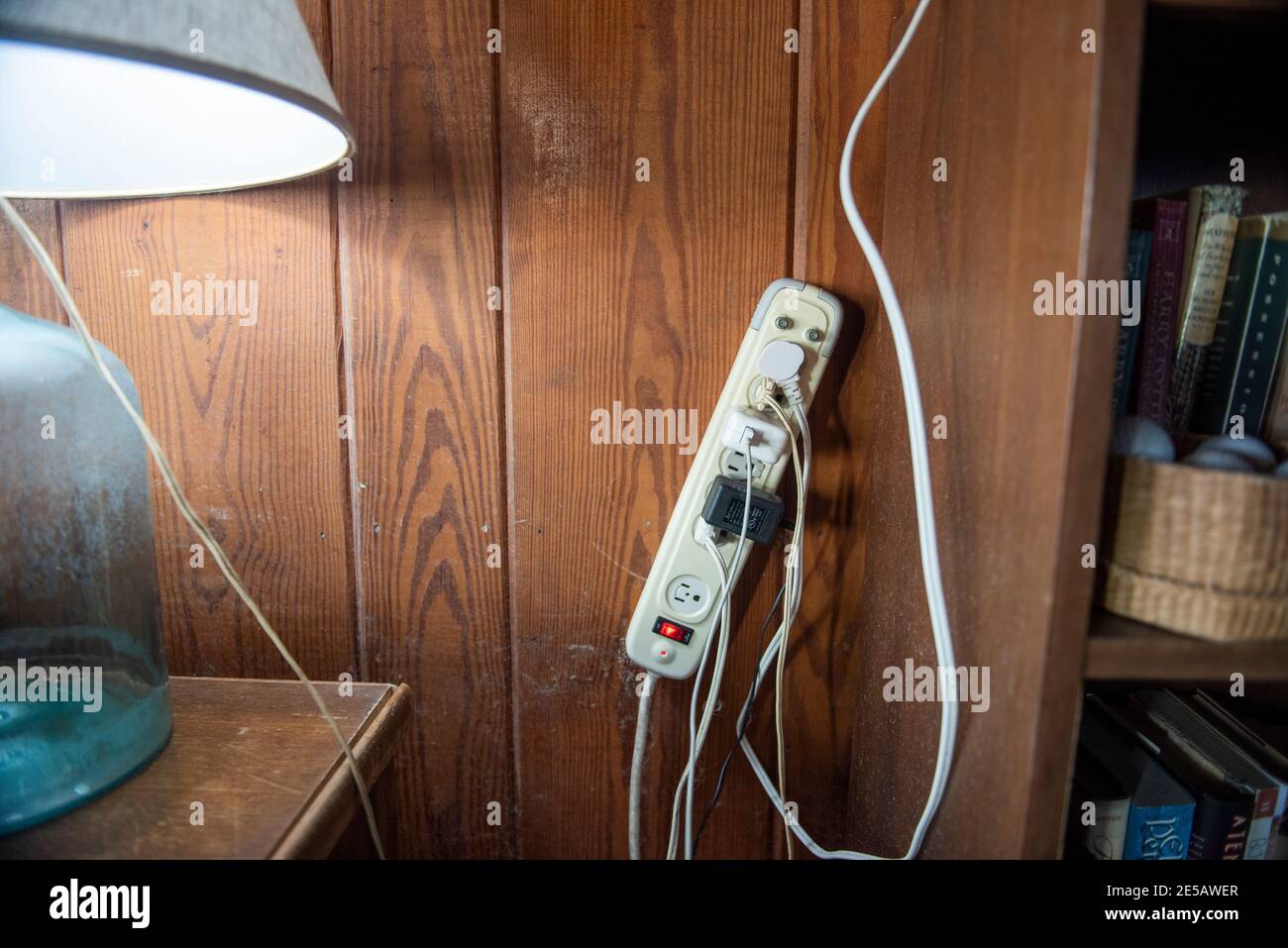 A surge protector with many cords plugged in is mounted on the wall. Stock Photo