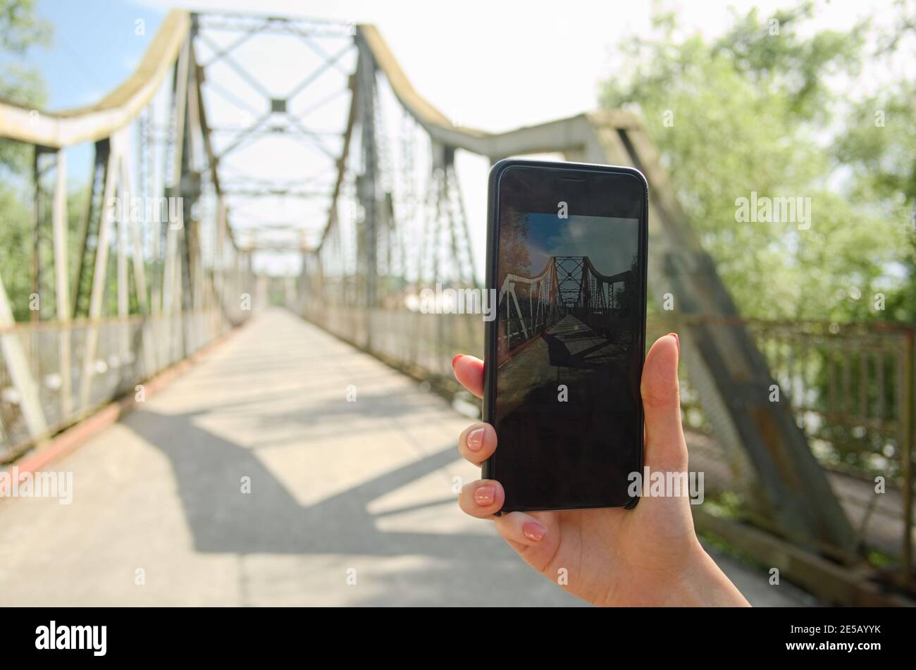 Girl hand holding phone and taking photo of the bridge. Tourist taking picture on cellphone. Stock Photo