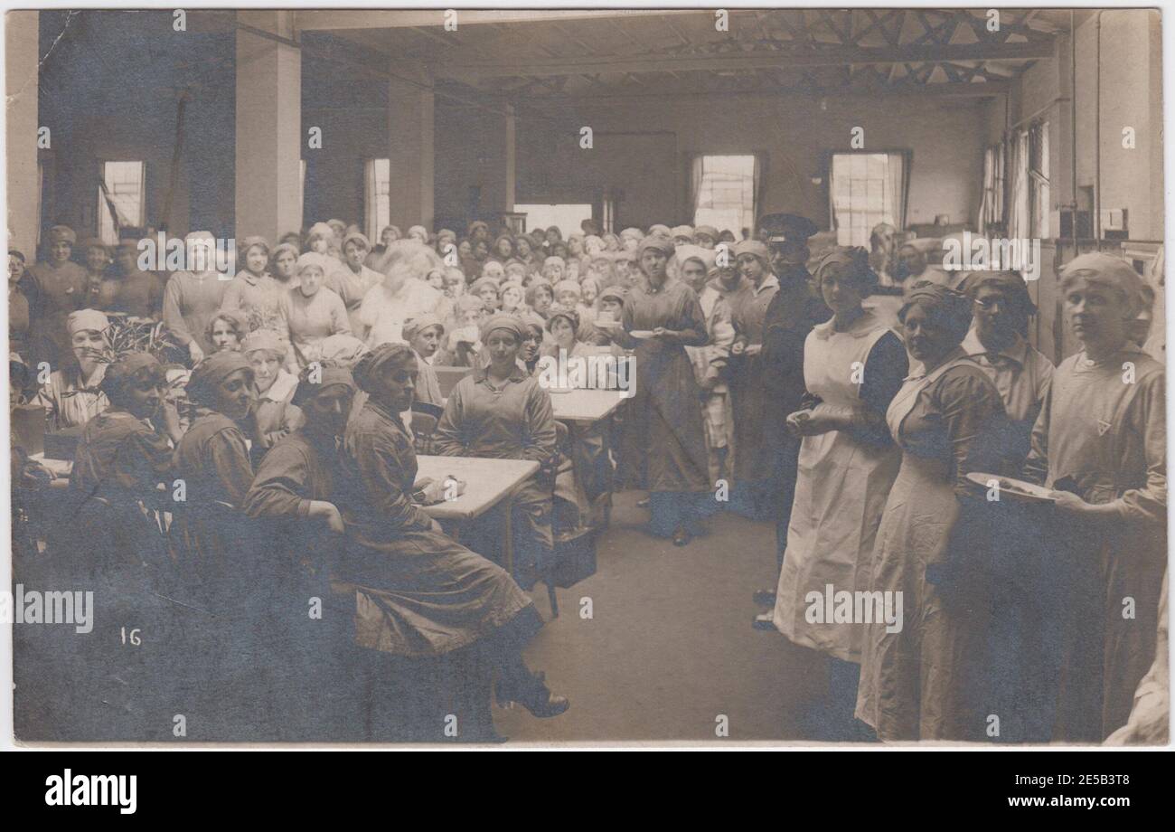 Packed munition workers' canteen during the First World War. The photograph shows women sitting at long tables, standing in a queue with plates and crowding around the room. One soldier is also standing with the women workers Stock Photo