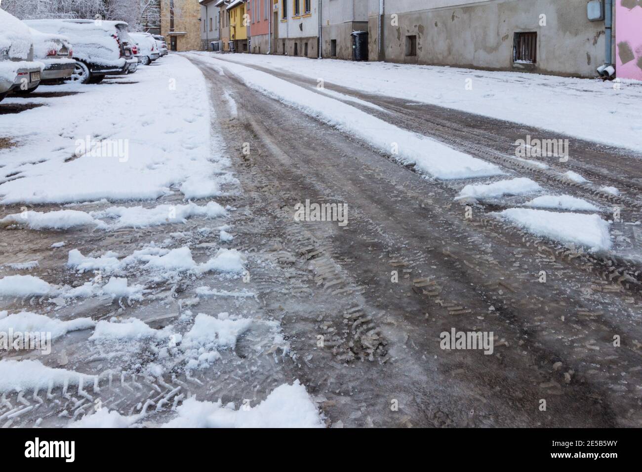 Street road covered with snow with car tracks, parking cars, row of houses, Sopron, Hungary Stock Photo