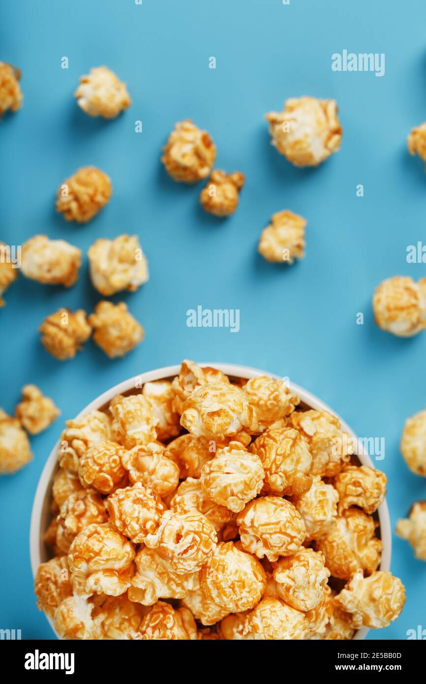 Caramel of the popcon in a white cup with a scissor on a blue background. Delicious catch for the films of movies, serials, cartoons. Free rightful, c Stock Photo