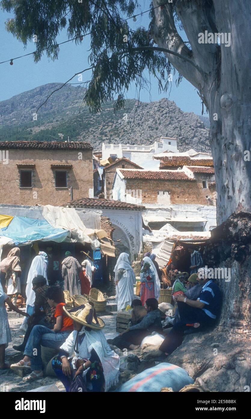 1984 Morocco Chefchaouen - Chefchaouen, Shafshāwan, also Chaouen, is a city in northwest Morocco. It is noted for its buildings in shades of blue. Chefchaouen is situated just inland from Tangier. The beauty of Chefchaouen's mountainous surroundings are enhanced by the contrast of the brightly blue painted medina (old town). Berber women in traditional hat and tourists in the Old town of Chefchaouen Morocco North Africa Stock Photo