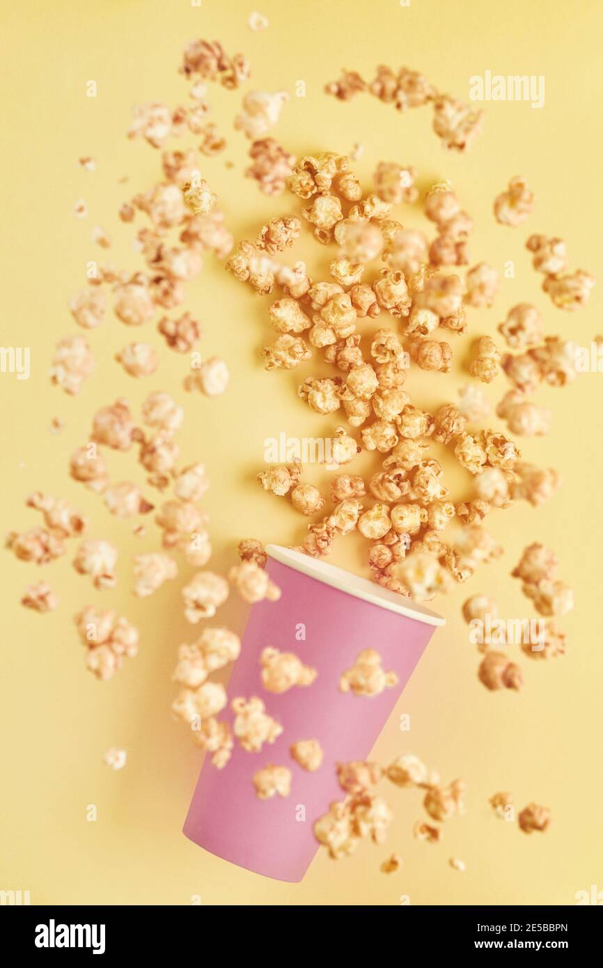 Flying delicious sweet popcorn with caramel in pink paper cup, isolated on trend color yellow background. Stock Photo