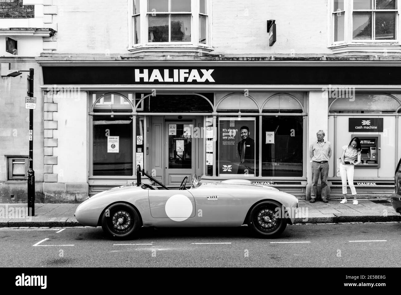 Two People Looking At and Photographing A Classic Sports Car Parked In The High Street, Lewes, East Sussex, UK. Stock Photo