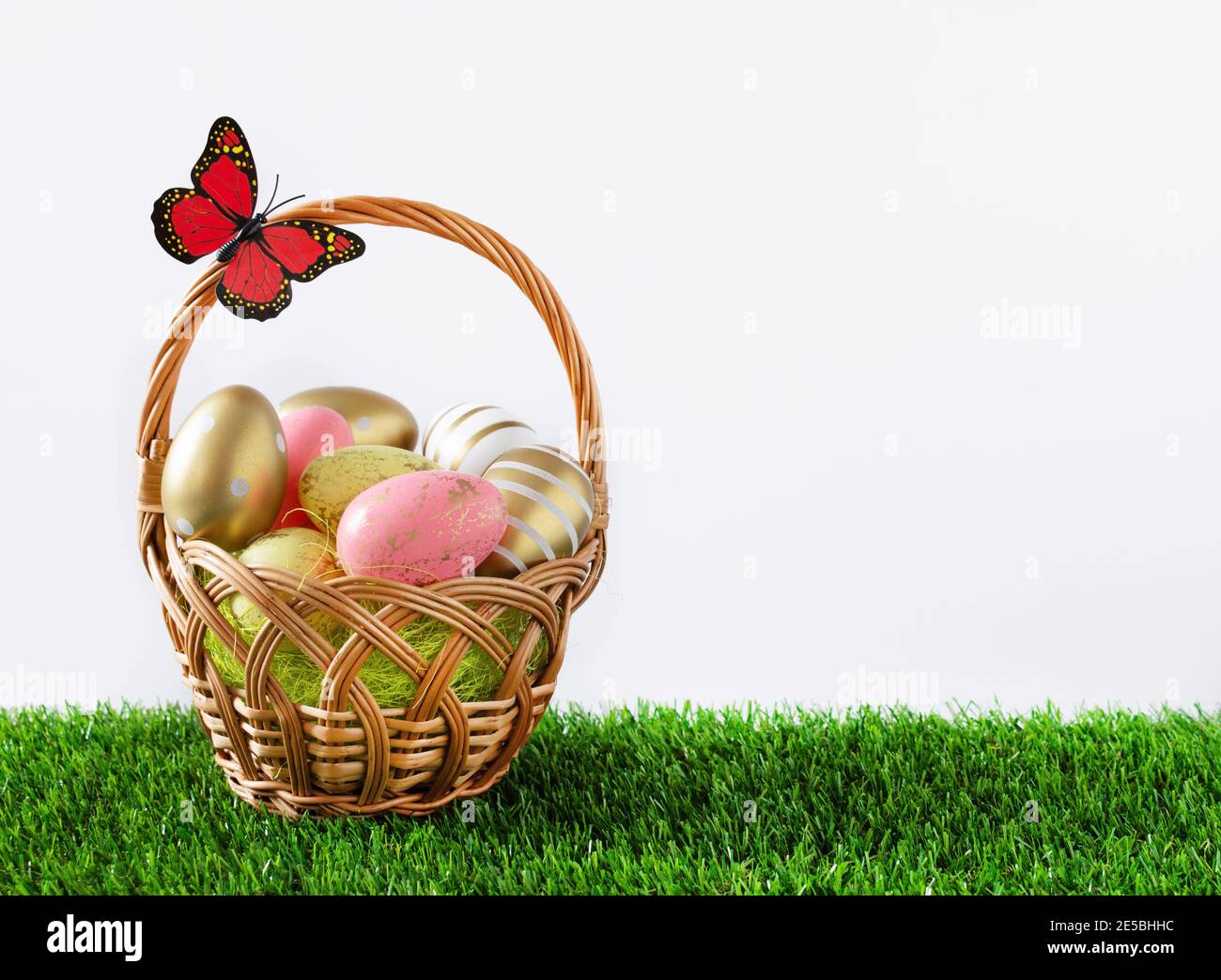 Basket full of multicolored easter eggs on green meadow over white background. Easter greeting card. Stock Photo