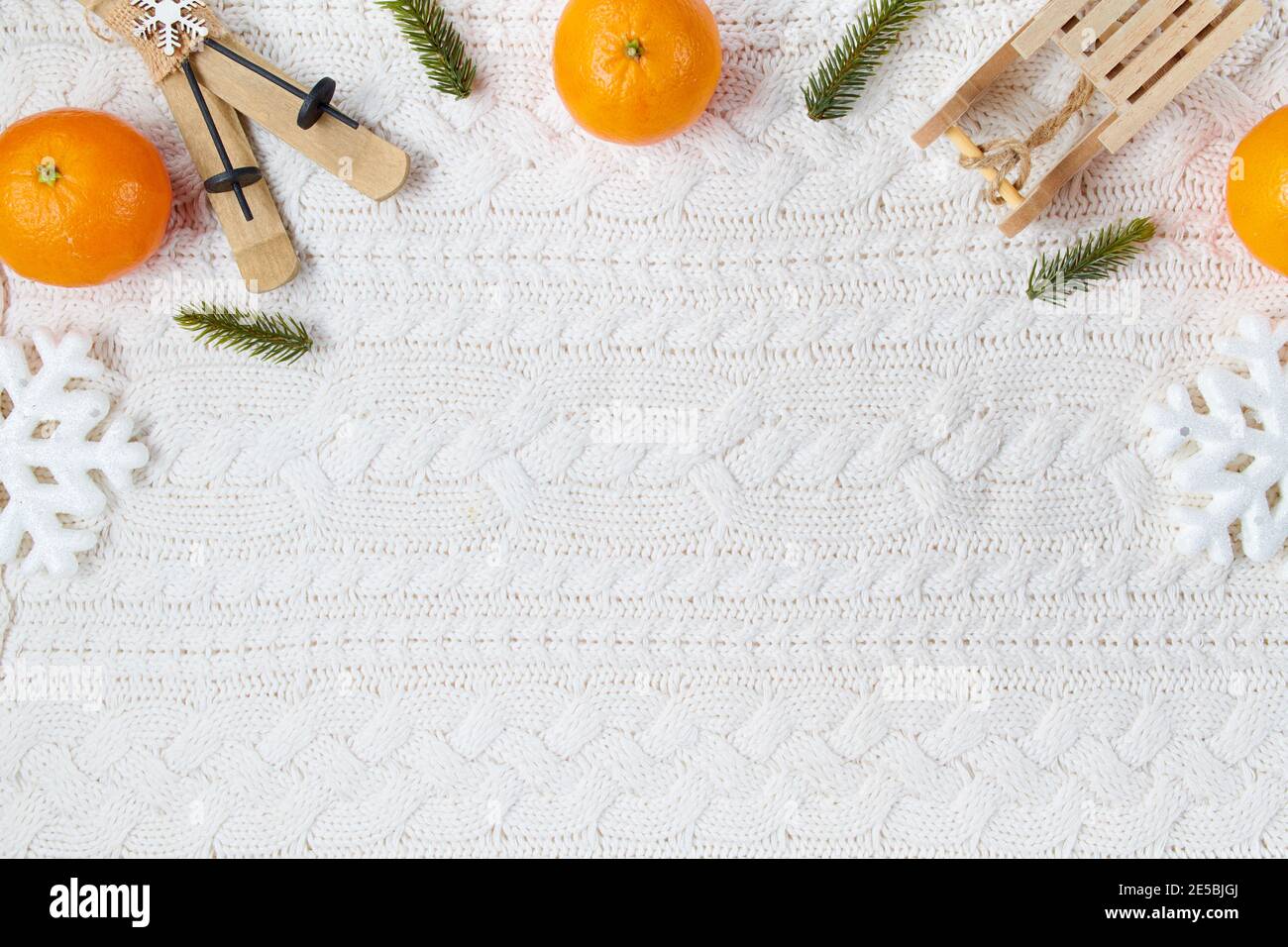 winter flat lay with snowflakes, mandarins, sleds and skis on white knitted background. Stock Photo