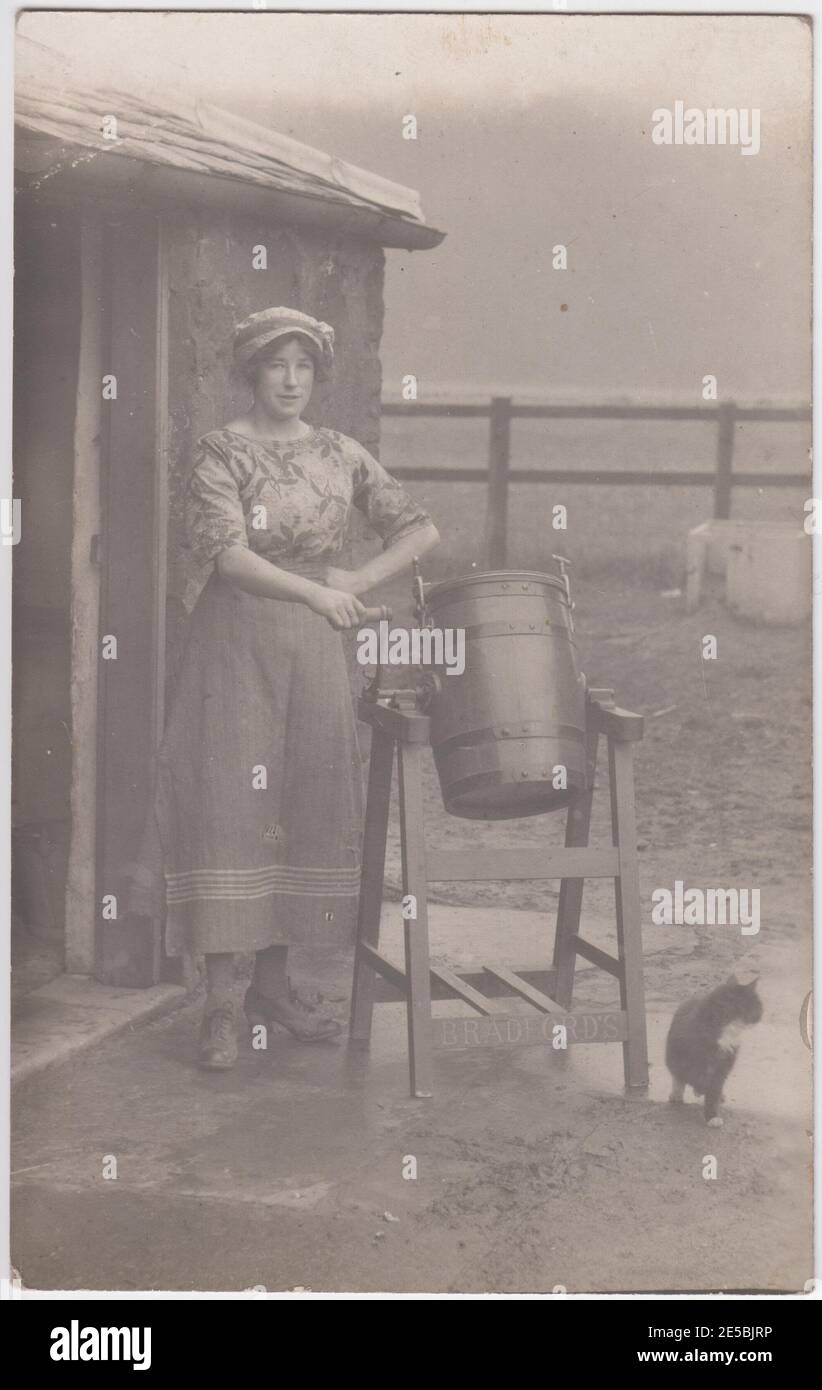 Woman standing in a farmyard next to a butter churn, the farm cat is next to her, 1900s / 1910s Stock Photo
