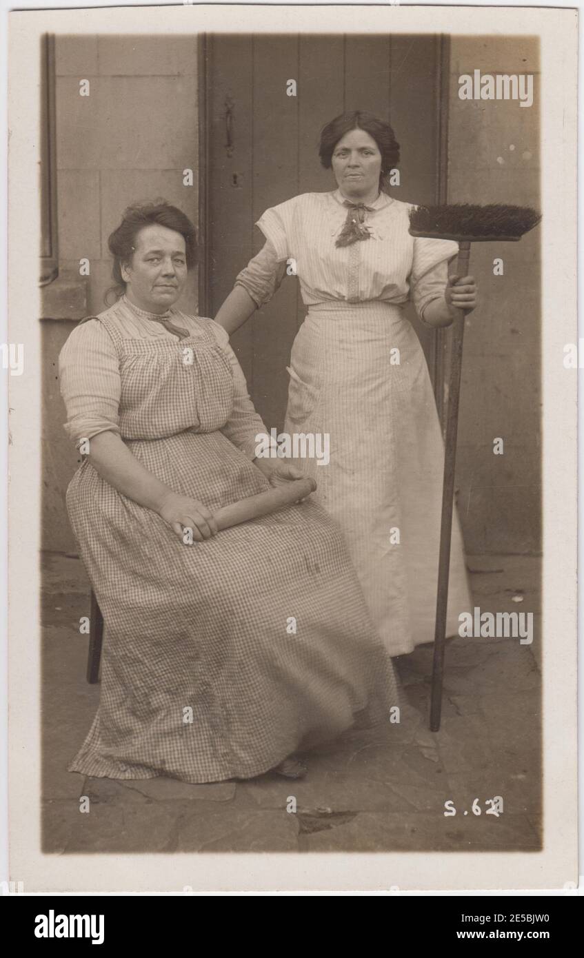 Two Edwardian female domestic servants, one holding a broom, the other wielding a rolling pin Stock Photo