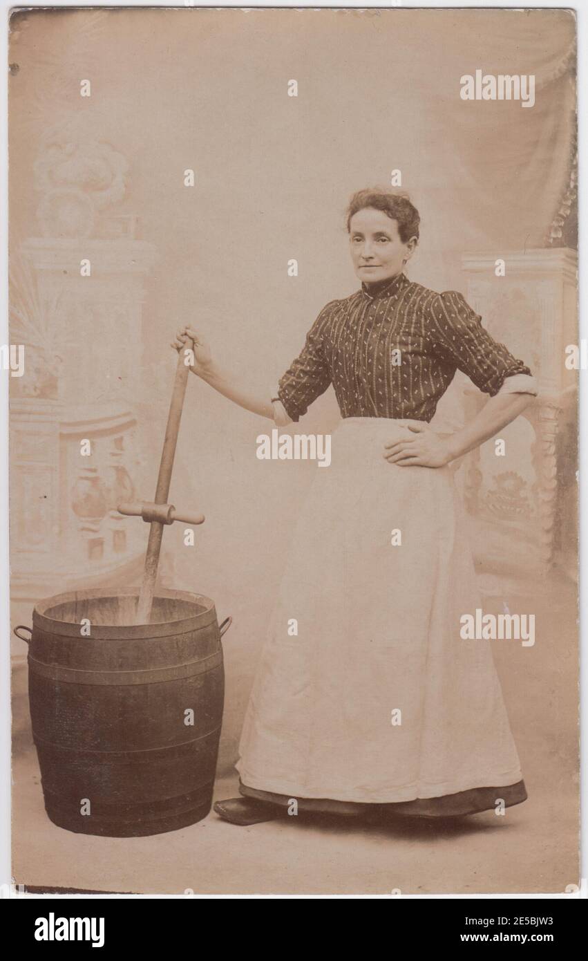 Edwardian servant shown with a washing tub and dolly. She is wearing an apron and posing with her hand on one hip. Stock Photo