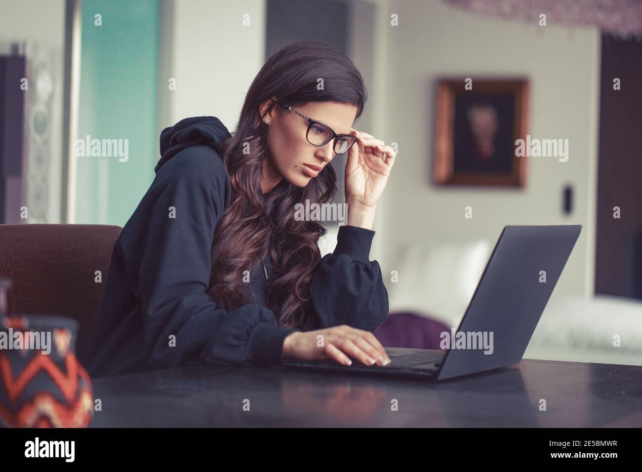 Young Caucasian woman with serious expression working on laptop in home office Stock Photo