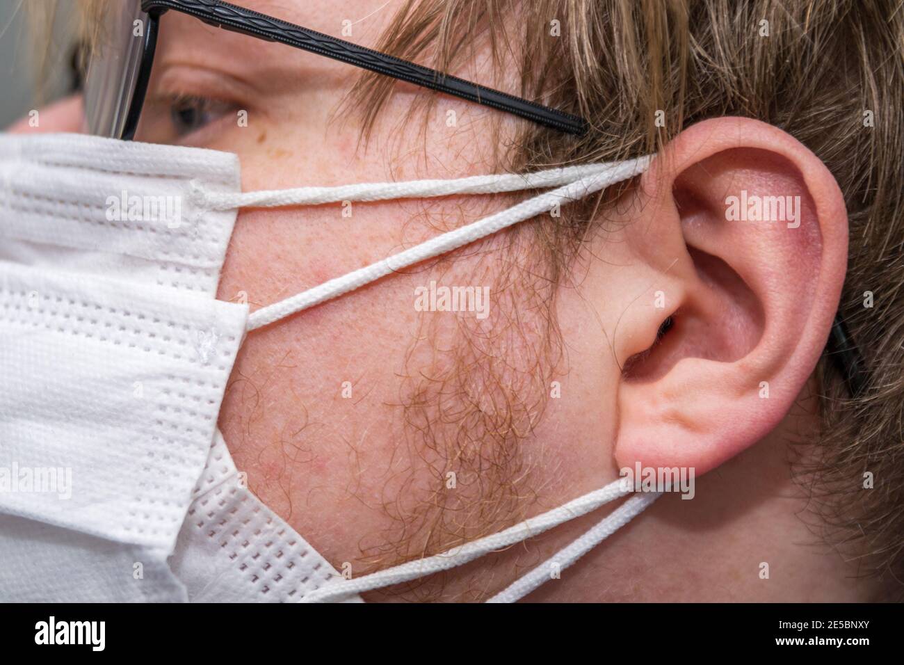 Man wearing two white facemasks for Covid-19 prevention; Round spectacles, white male, blond hair. Side view, zoomed. Stock Photo