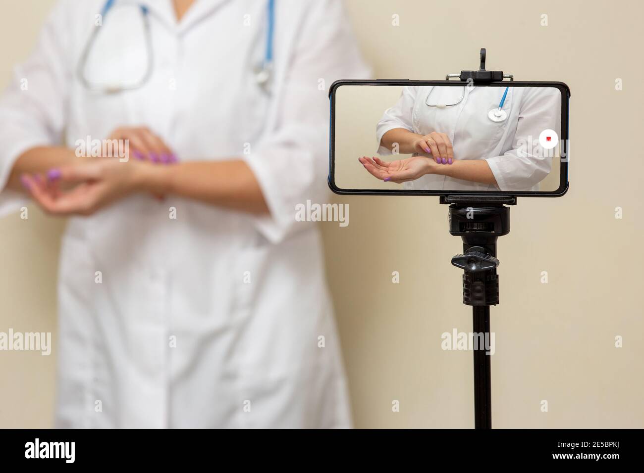 A woman doctor records a video on a smartphone, how to measure the pulse on her arm. Stock Photo
