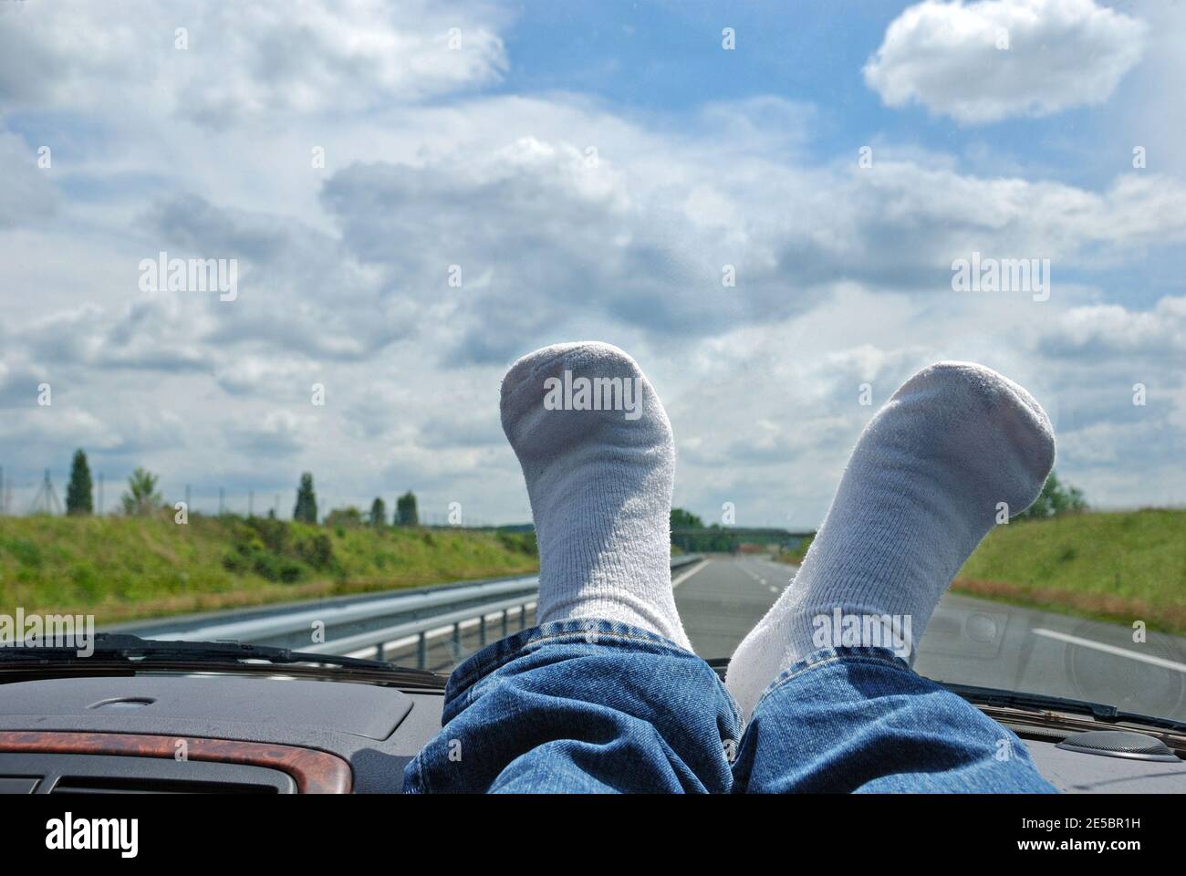 Feet in white socks on car's dashboard, driving on empty highway Stock