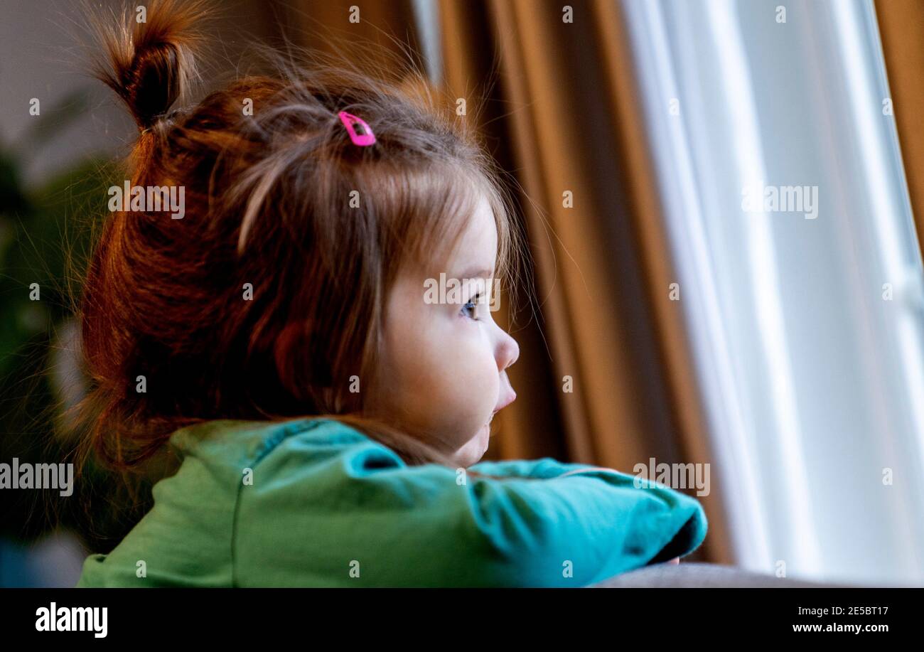 Small child looks out of the window on a cloudy winter day Stock Photo