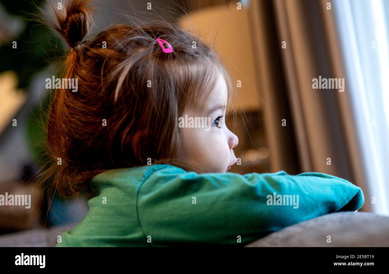 Small child looks out of the window on a cloudy winter day Stock Photo