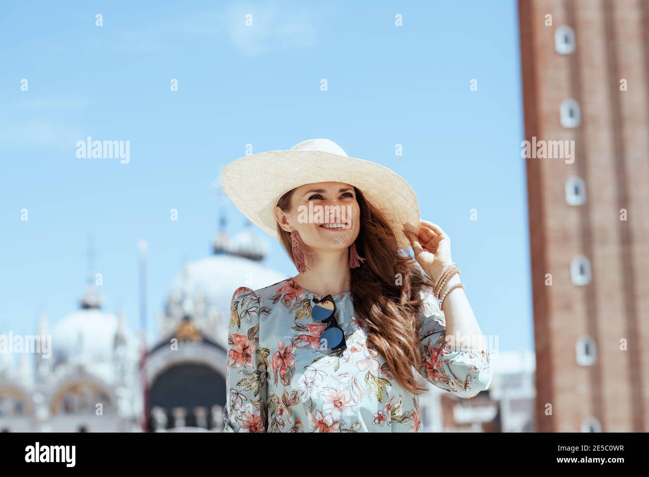 happy stylish solo tourist woman in floral dress with sunglasses and hat having excursion at San Marco square in Venice, Italy. Stock Photo