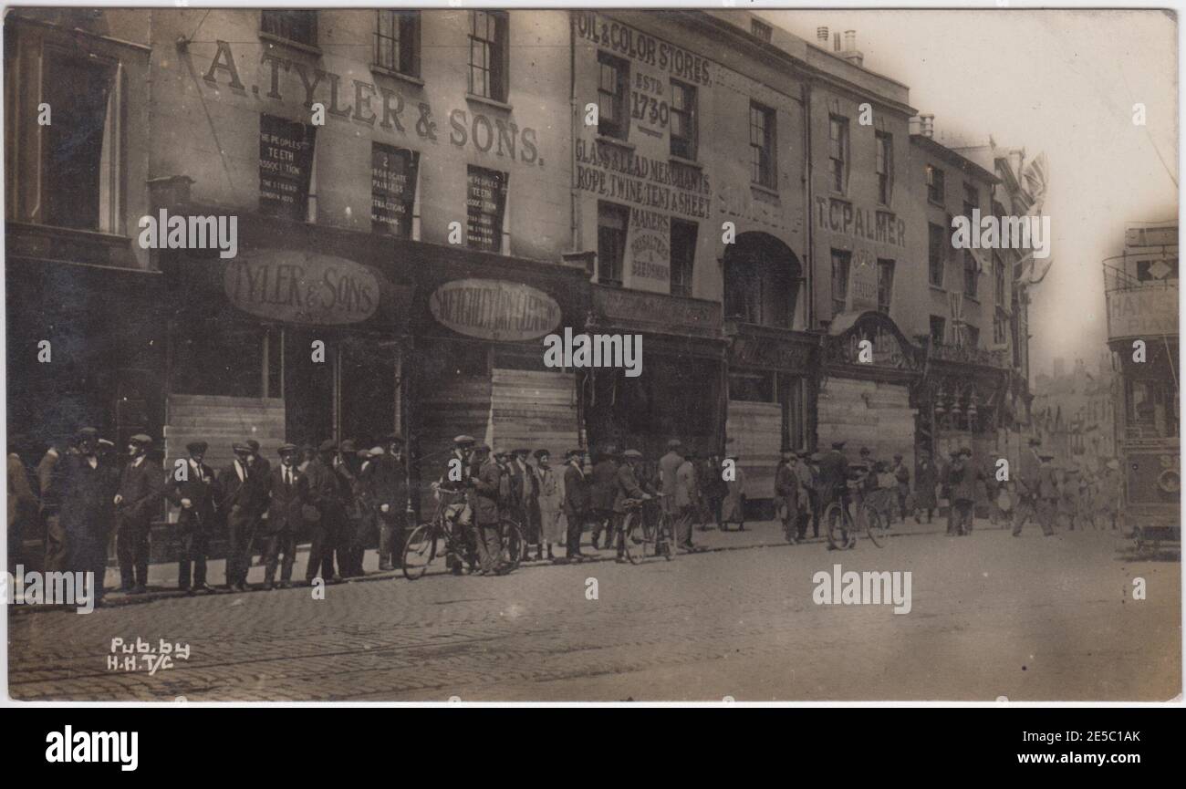 Broadway, Coventry, seen in the aftermath of the 1919 hunger riots. Rioting broke out in Coventry following celebrations to mark Peace Day (and the end of the First World War) in July 1919. The image shows a crowd of men, most wearing flat caps, some with bicycles, lined up in the street. Most of the shops have windows boarded up. Stock Photo