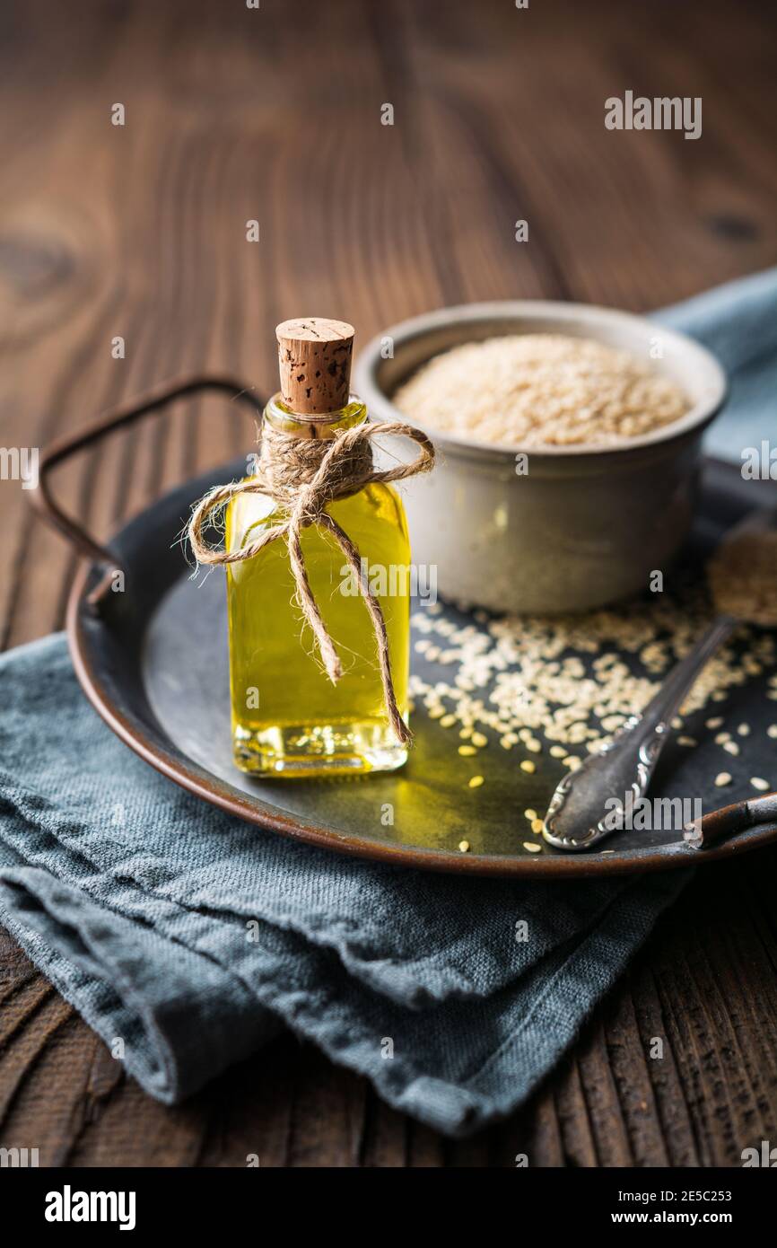 Healthy cold pressed sesame oil in a glass bottle and seeds in a bowl on wooden background Stock Photo