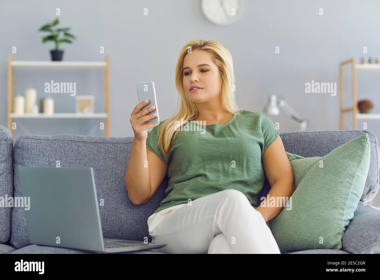 Woman working from home using laptop computer while reading text message on mobile phone. Stock Photo