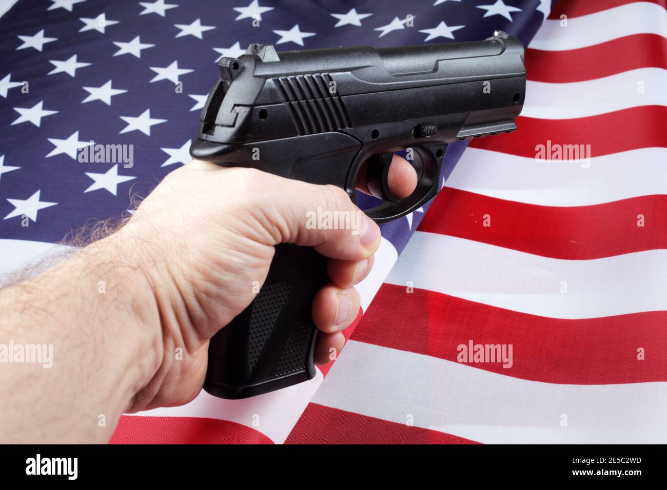 Pistol in a man's hand against the background of the American flag, selective focus. Stock Photo