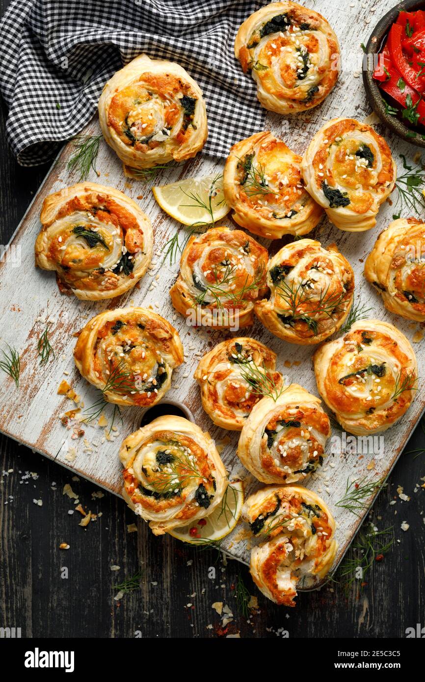 Puff Pastry Pinwheels stuffed with salmon, cheese and spinach served on a board on a black wooden table top view Stock Photo