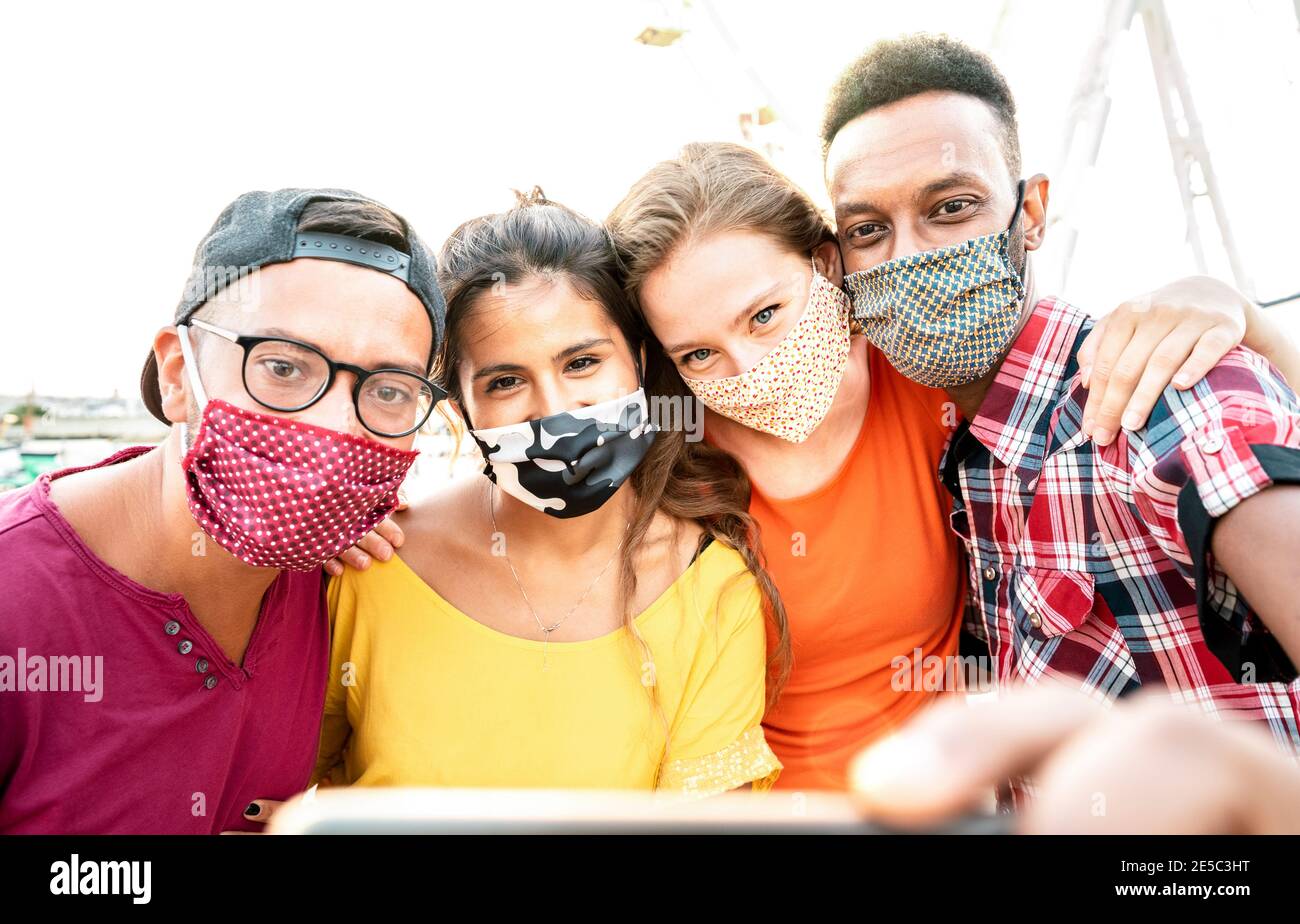 Multicultural milenial travelers taking selfie with closed face masks - New normal travel concept with young people having safe fun together Stock Photo