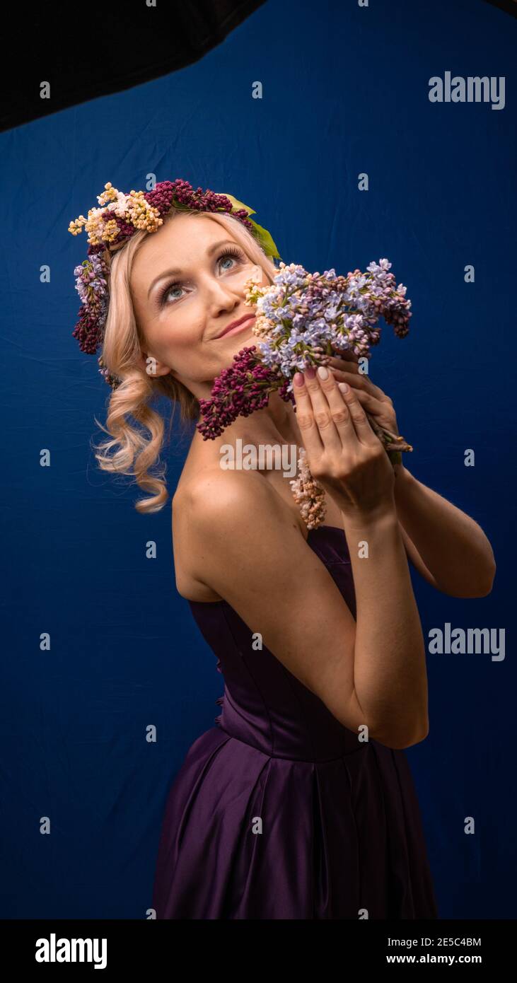 Auspicious beautiful girl in a lilac wreath with a charming smile rejoices on a blue background, happy day Stock Photo