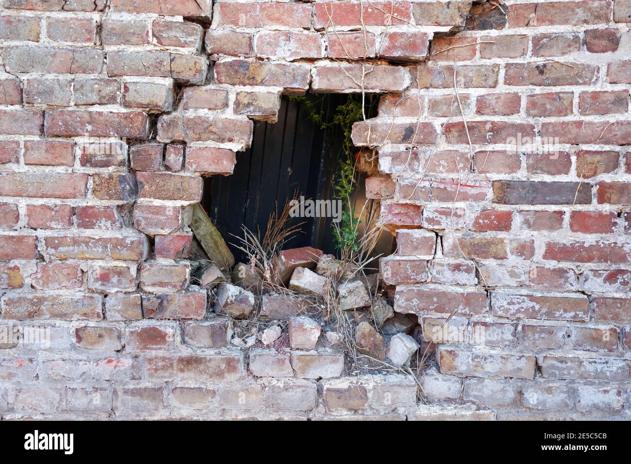 Photograph of a broken porous old ruined brick wall Brick wall with hole after accident, many cracks, collapse hazard, dark background, horizontal Stock Photo