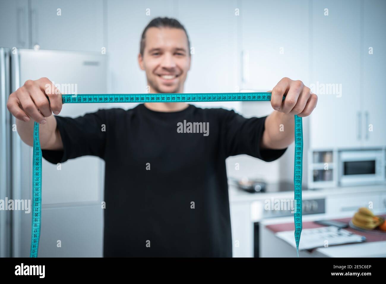 happy attractive fitness nutritionist man with measuring tape at modern kitchen Stock Photo