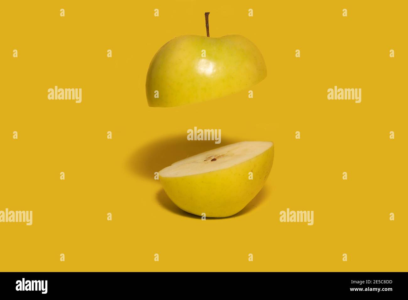 Green apple sliced in half with one half floating in air. Dark yellow background. Creative fruit concept Stock Photo