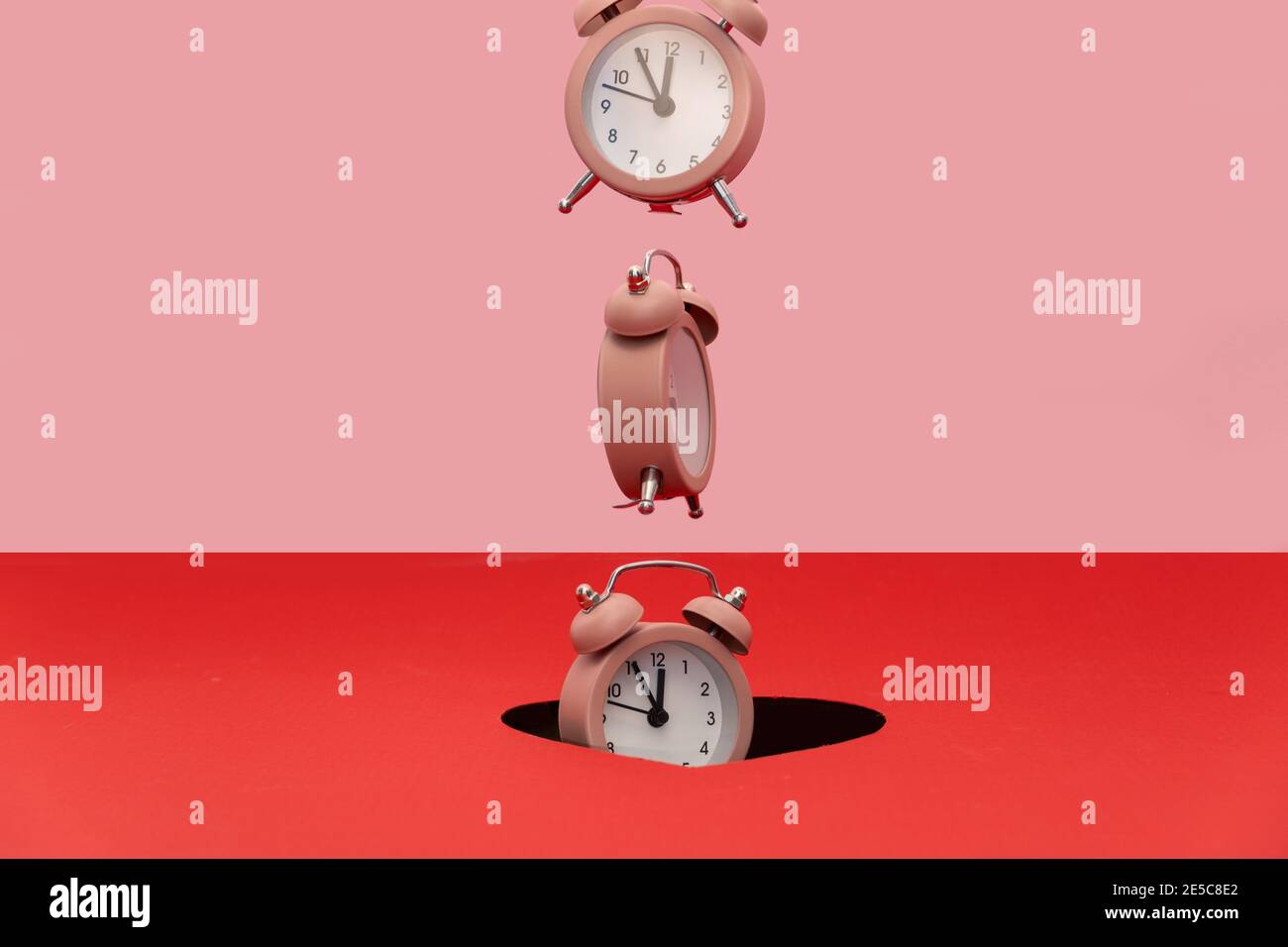 Alarm clock is falling trough the hole. Dual tone background. Creative time concept Stock Photo