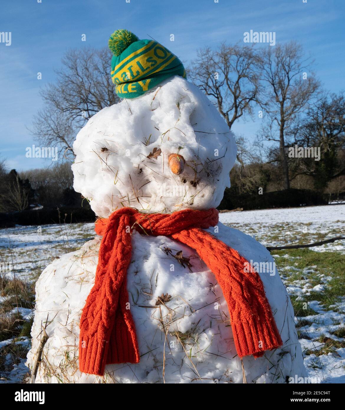 Winter scene of a  snowman  on a village green , Oxfordshire ,  wearing a football supporters beany Stock Photo