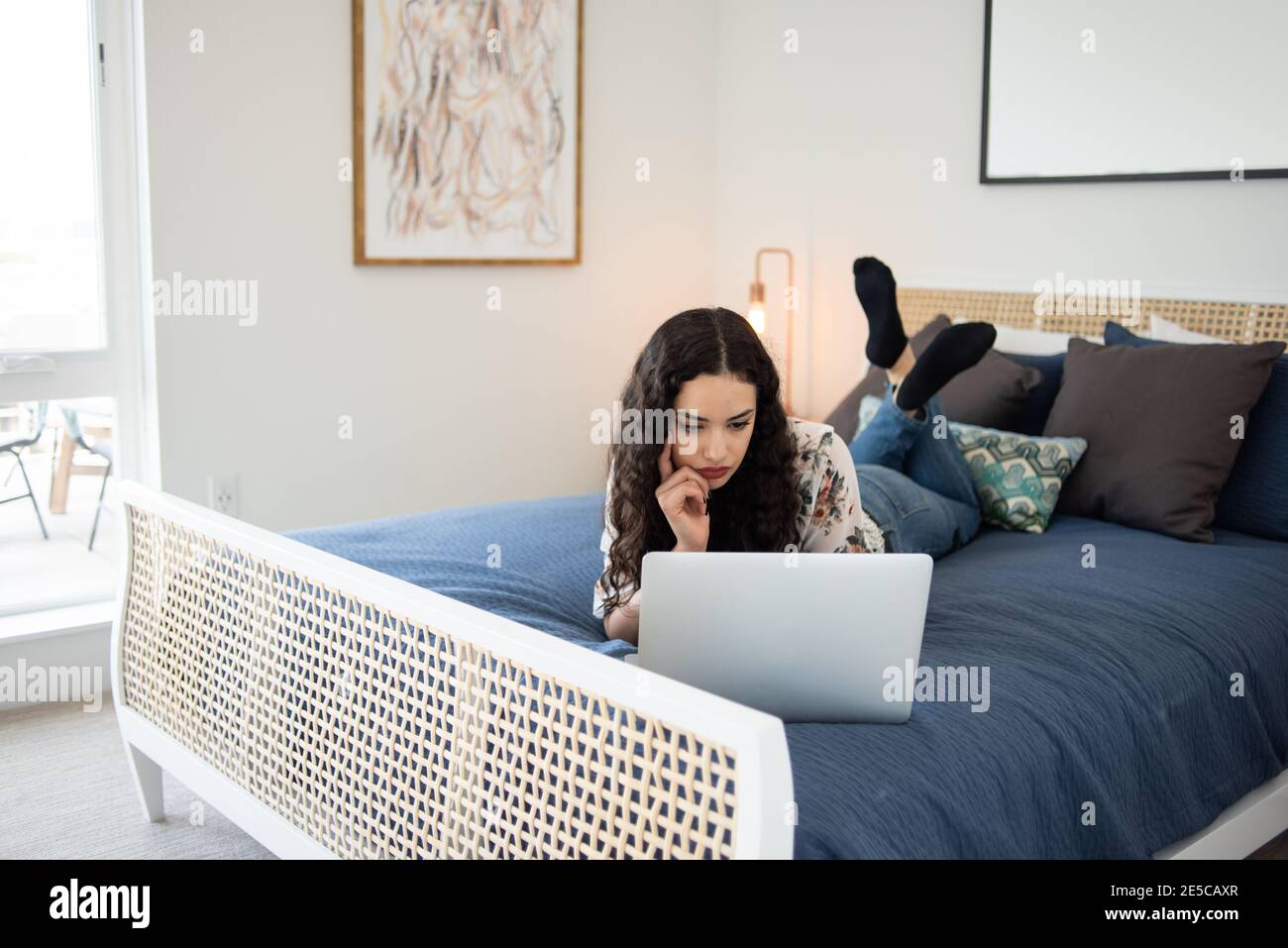 Young woman lying on bed looking at laptop Stock Photo