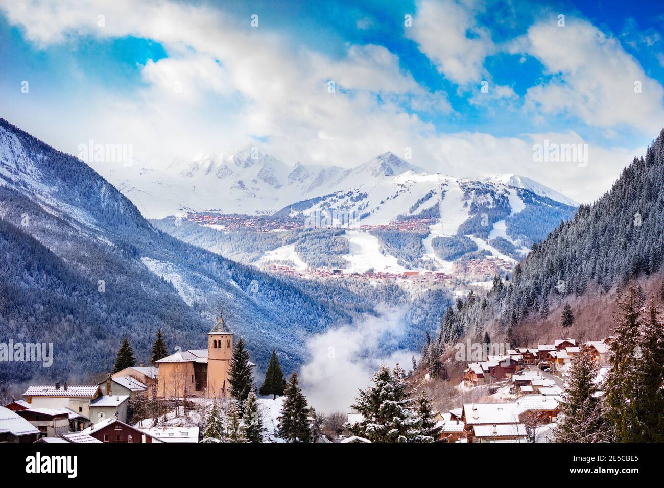 Panorama of Champagny-en-Vanoise village with mist and clouds around old church, over Courchevel resort on background Stock Photo