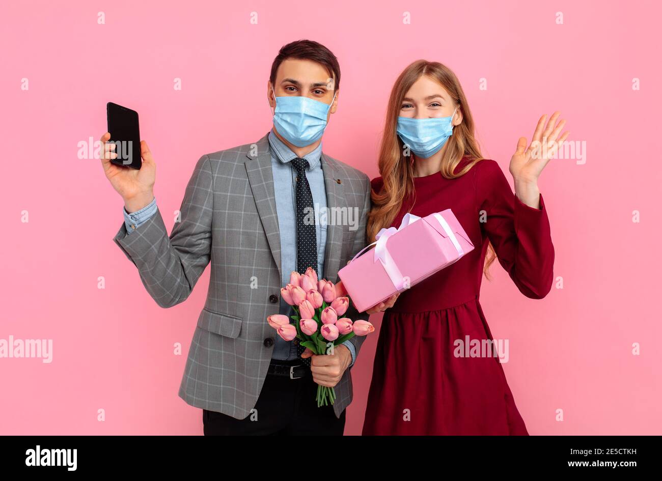 https://c8.alamy.com/comp/2E5CTKH/excited-young-couple-wearing-medical-masks-celebrating-valentines-day-with-gift-box-and-flowers-using-mobile-phone-on-pink-background-2E5CTKH.jpg