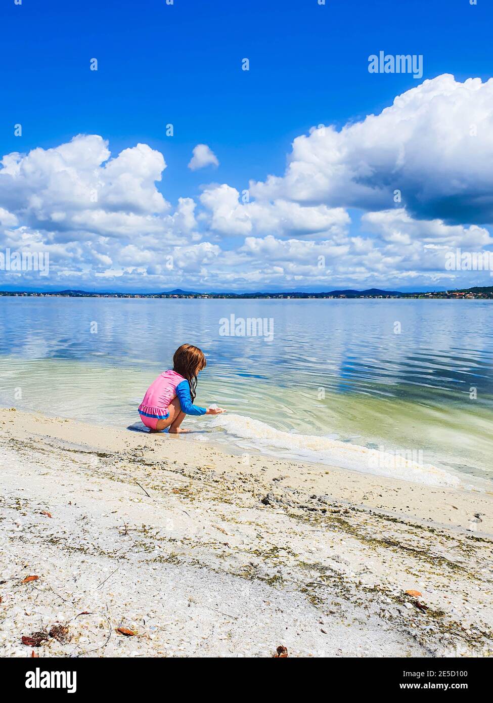 Girl crouching on beach playing with sand, Rio de Janeiro, Brazil Stock Photo