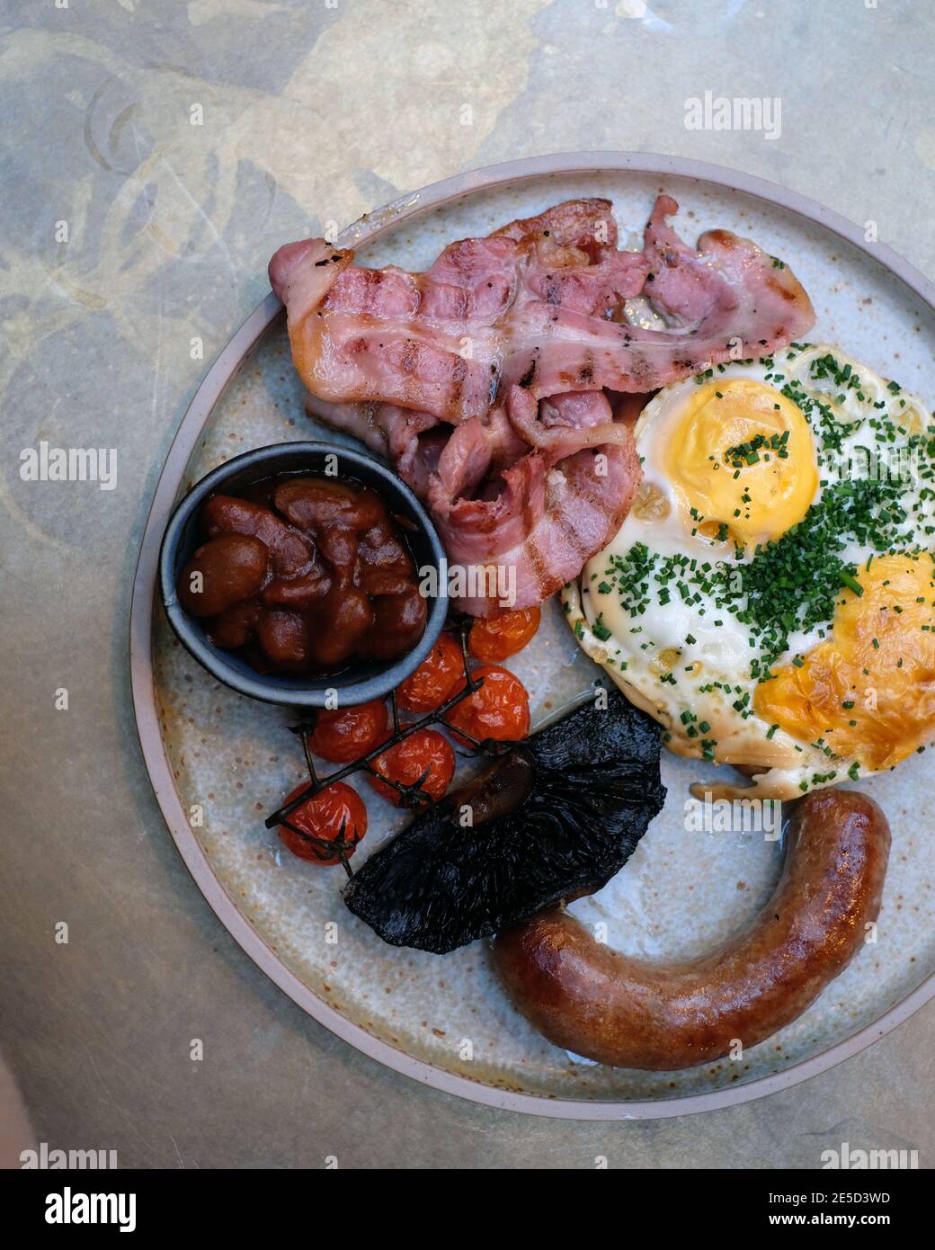 Full English Breakfast with fried eggs, bacon, roasted tomatoes, roasted mushrooms, baked beans, parsley and pork sausage Stock Photo