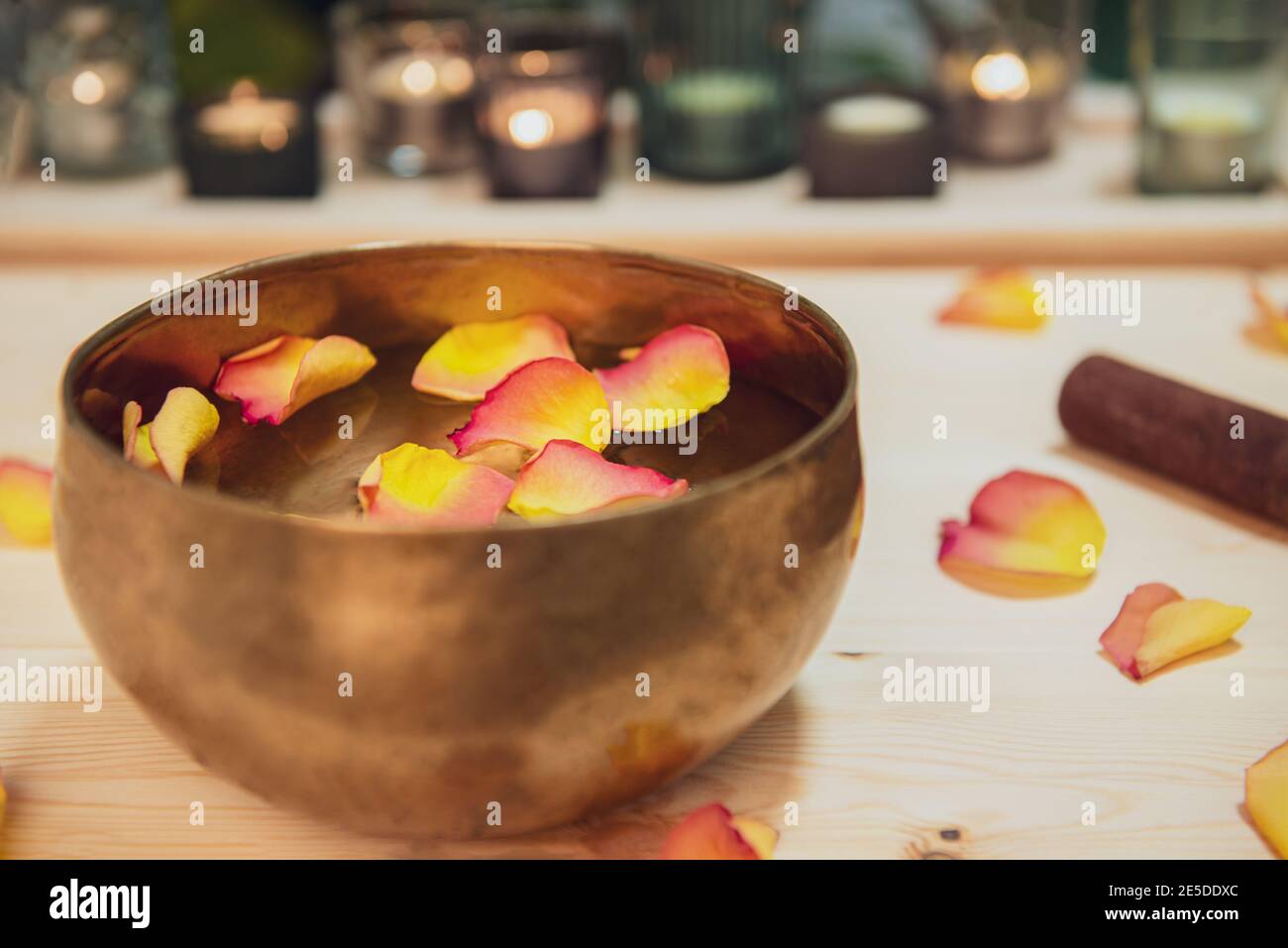 Tibetan singing bowl with floating in water flower petals. Special sticks, burning candles, petals on the wooden background. Meditation and Relax Stock Photo