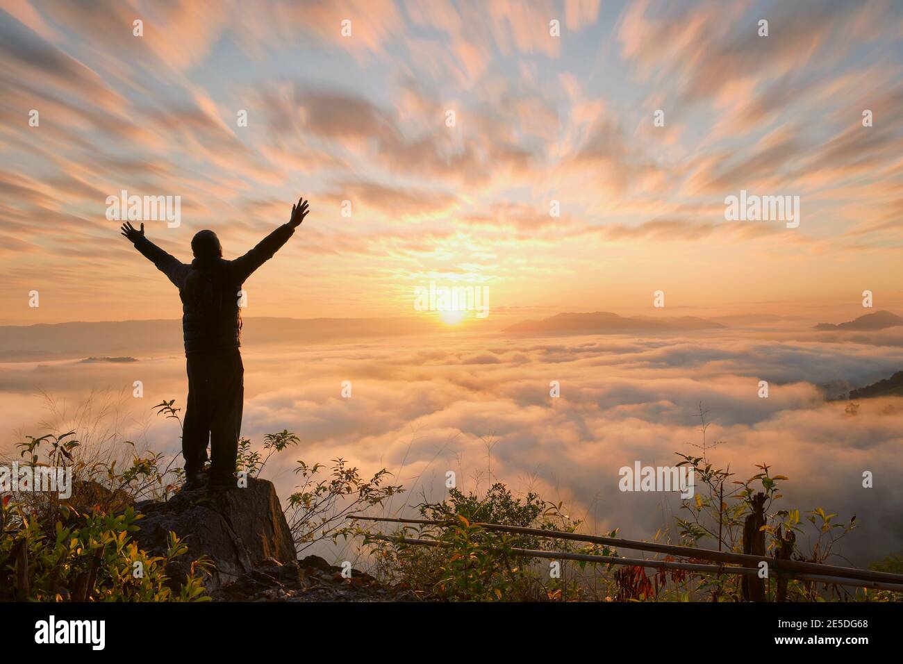 Silhouette of a man standing on a mountain with his arms outstretched ...