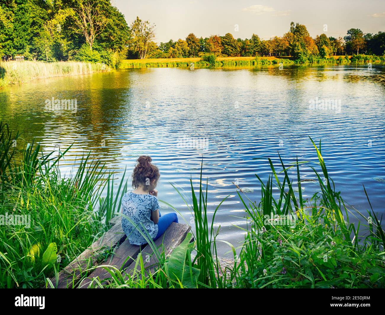 Rear view of a girl sitting by a lake, Poland Stock Photo