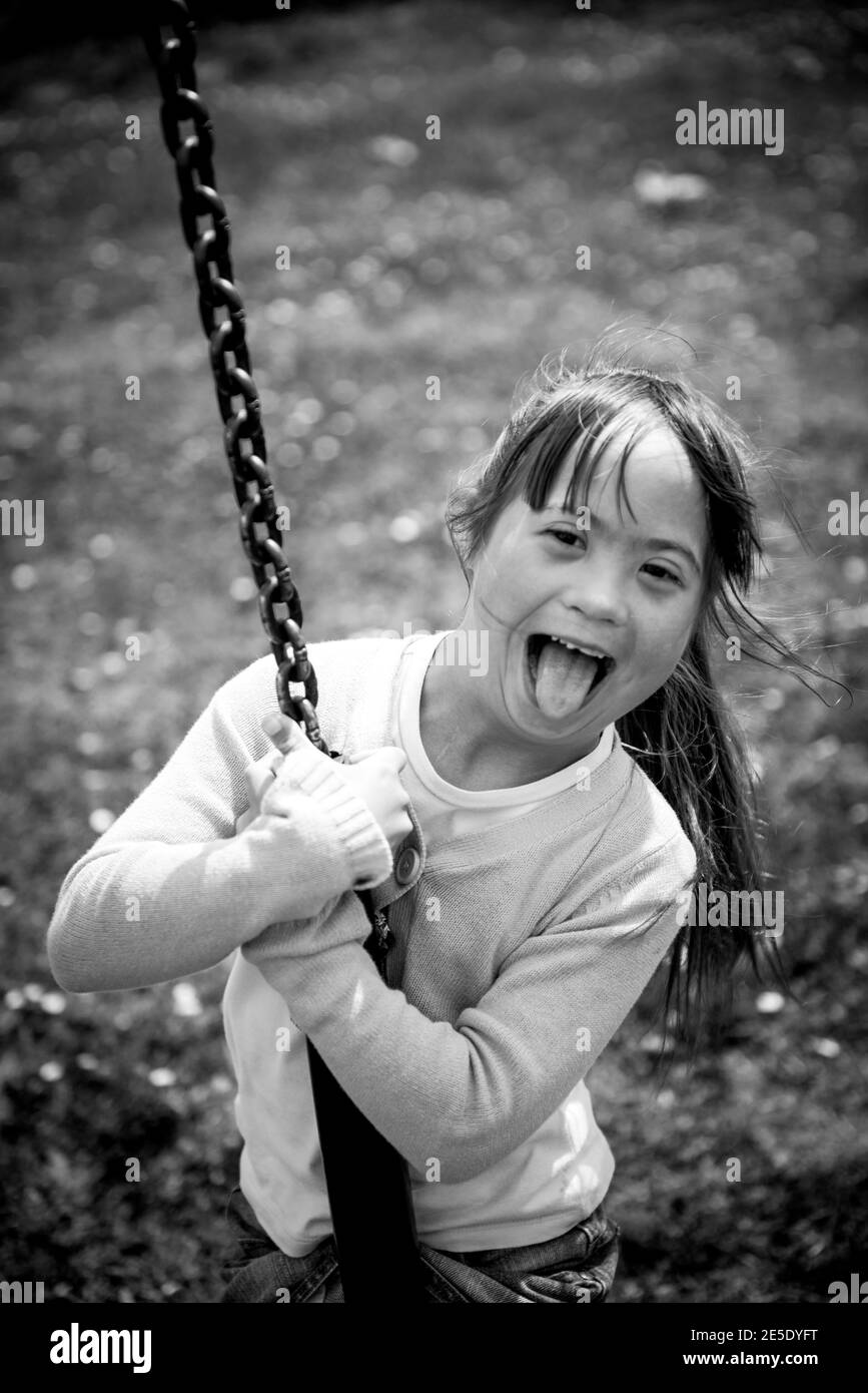 Happy little girl with Downs Syndrome playing on a rope swing at a park Stock Photo